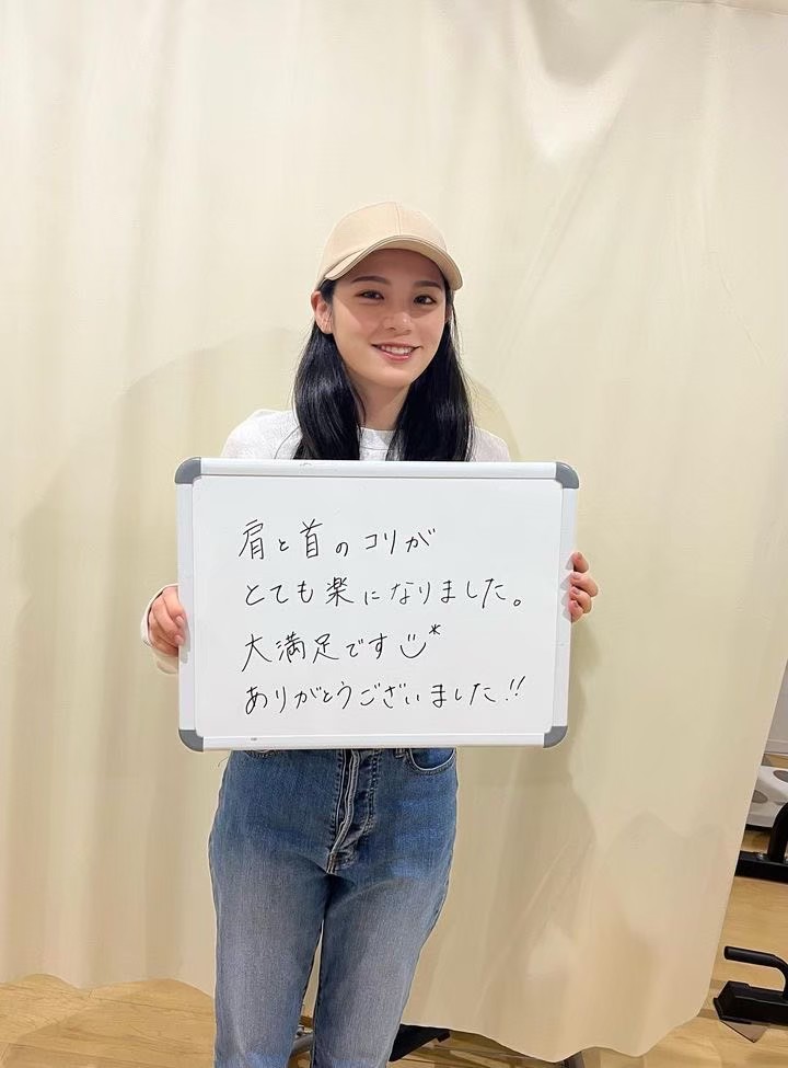 肩と首のこりが楽になったと書かれたホワイトボードを持つお客様